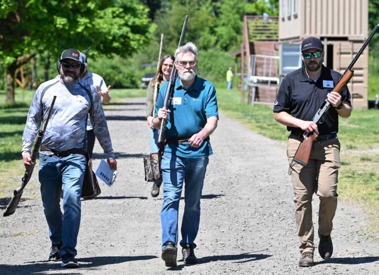 three men wearing shooting gear carrying rifles