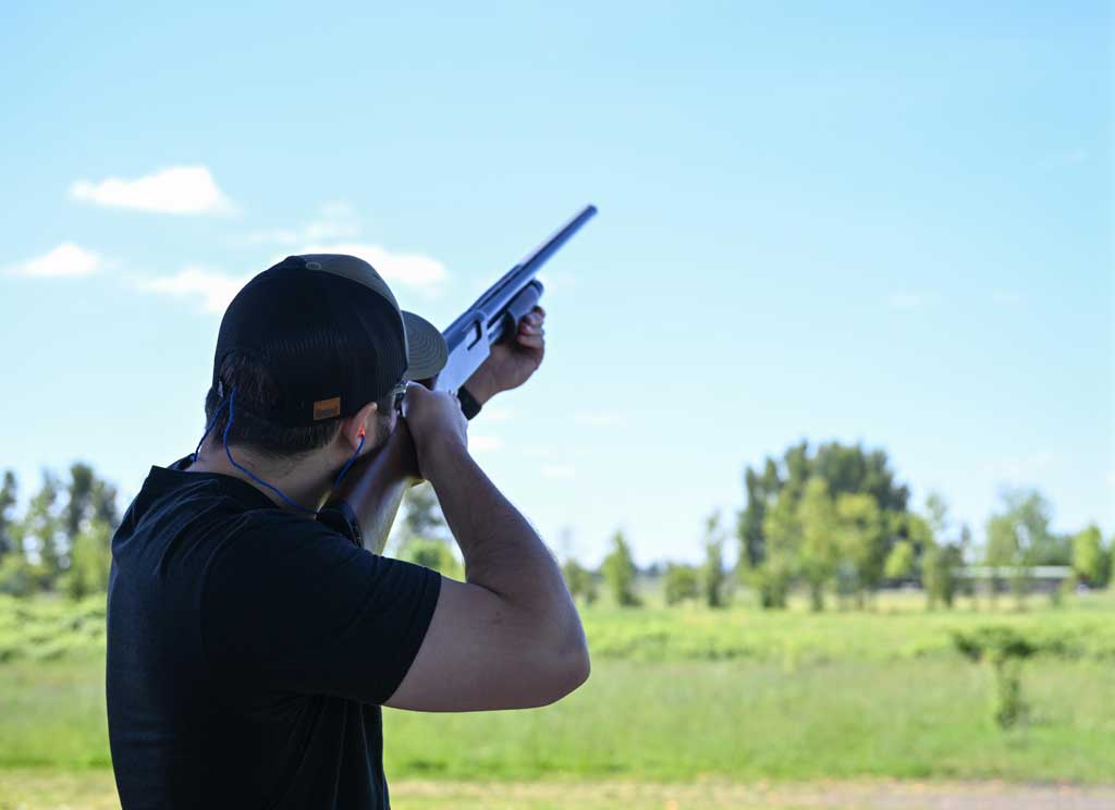 man holding rifle shooting at a clay